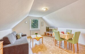 Une chambre mansardée chaleureuse, avec un plafond en pente, un lit, une petite table sur laquelle est posé un vase, et une vue sur les arbres par la fenêtre.