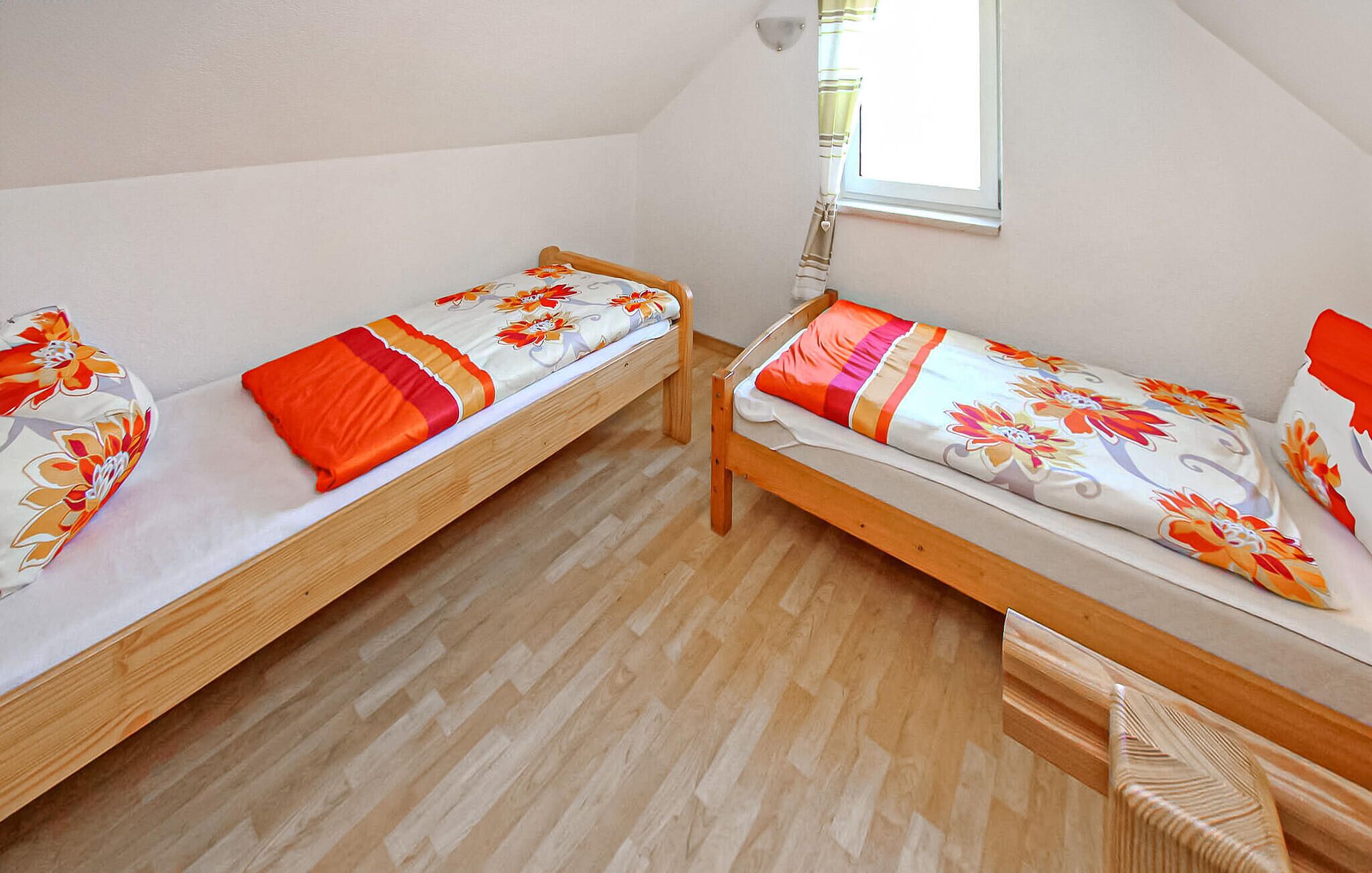 A dormitory room with two wooden bunk beds, each with floral bedding and orange accents.