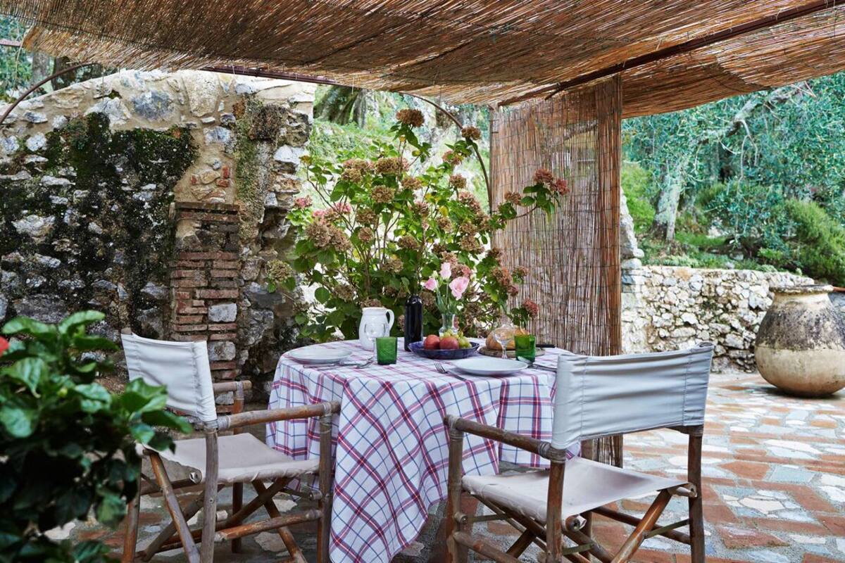 An outdoor dining area with a checkered tablecloth, wicker chairs, and a rustic stone wall backdrop.