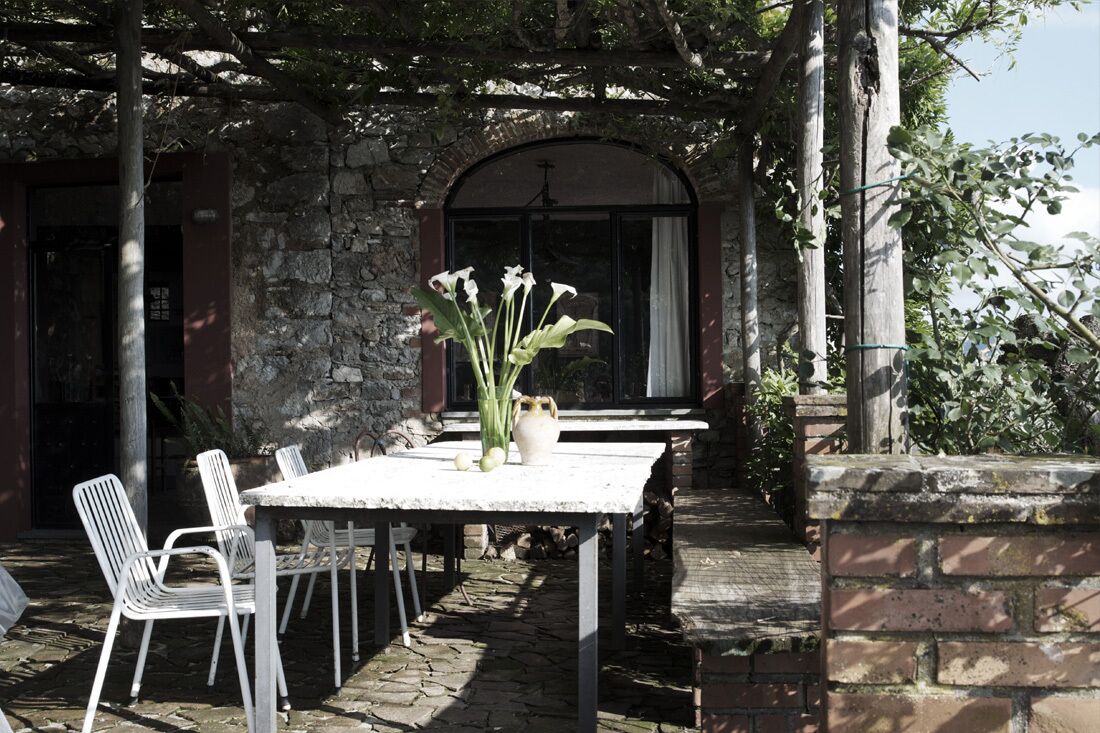 Un patio exterior con un muro de piedra, una mesa con sillas y un jarrón con flores.