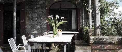 Un patio exterior con un muro de piedra, una mesa con sillas y un jarrón con flores.