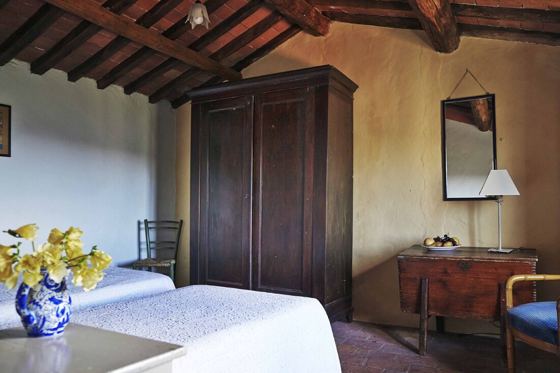 A room with two beds, a wooden wardrobe, a desk with a lamp, and a mirror on the wall.