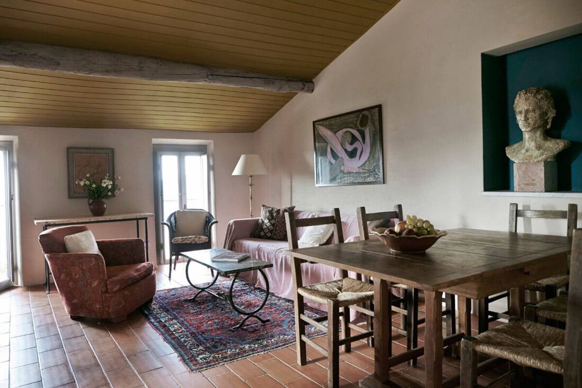 A dining area with a wooden table, chairs, and a vase of fruit. There is a window with a view of the outside.