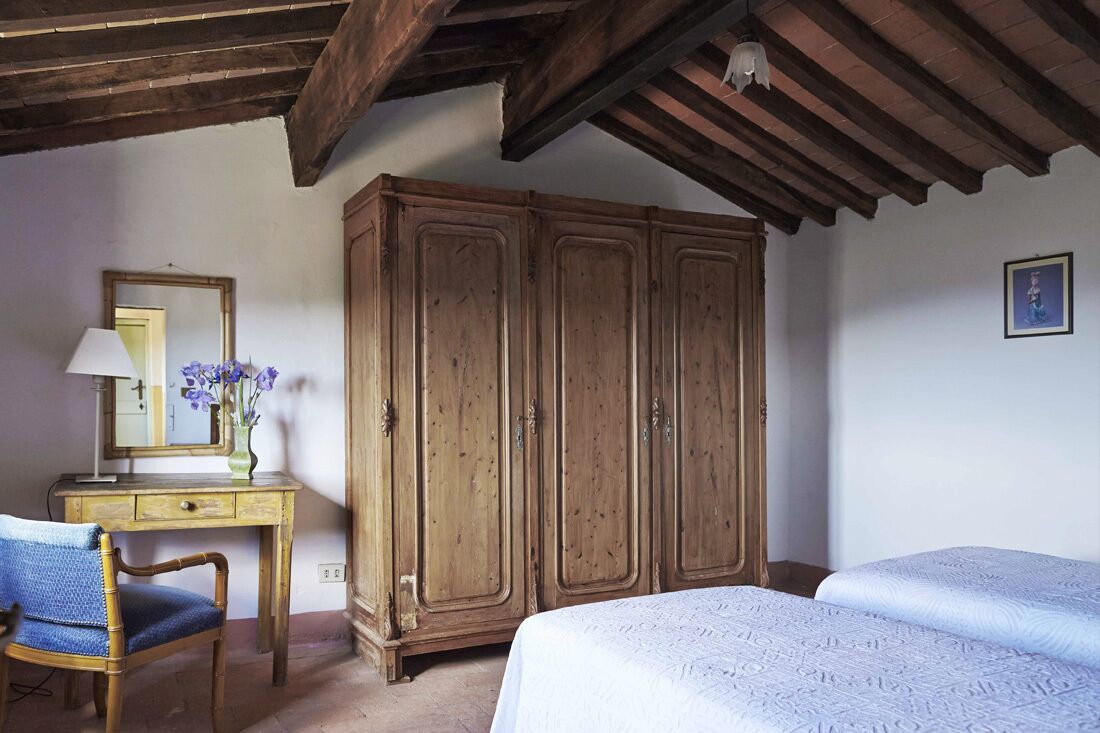 Un dormitorio con un armario de madera, un escritorio con espejo y una cama con colcha blanca.