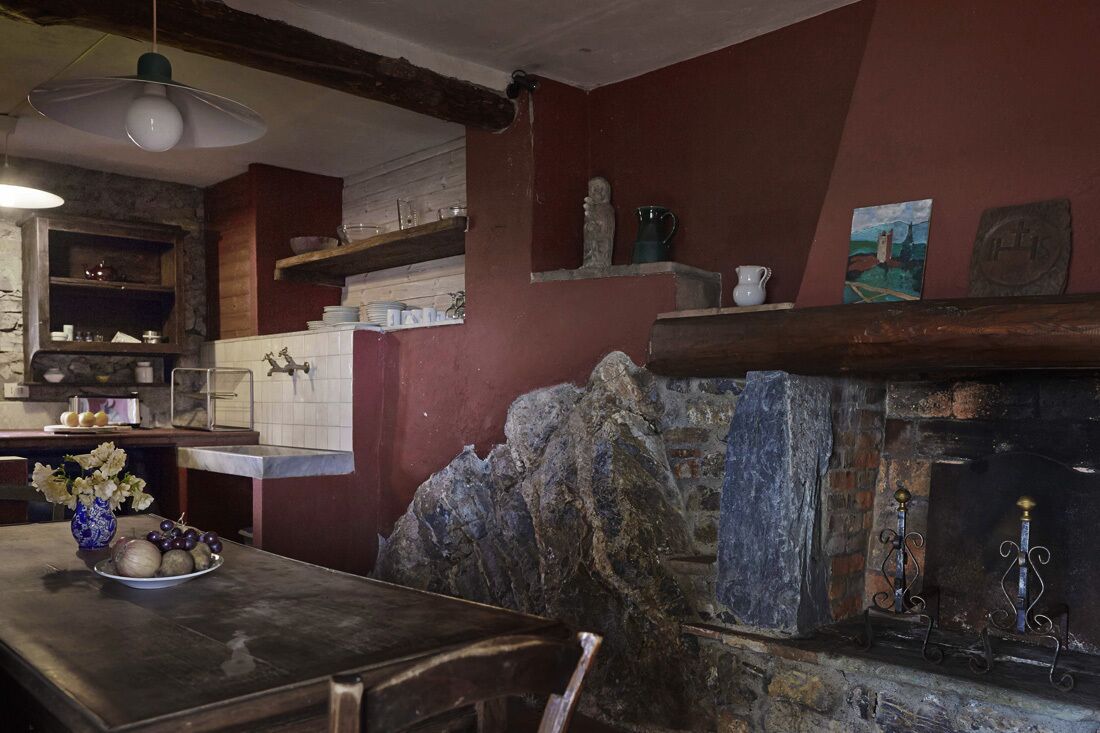 A rustic kitchen with stone walls, wooden beams, and a stone fireplace.