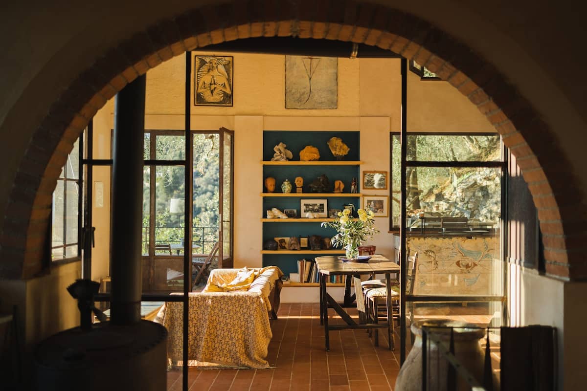 A cozy room with a brick archway, a fireplace, a bookshelf, and a window with a view of greenery.