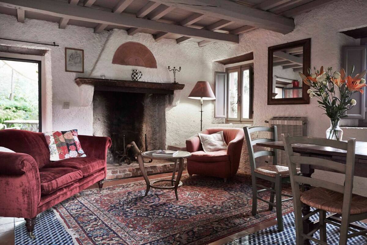 A cozy living room with a fireplace, red sofas, a round table, and a dining area with wooden chairs.