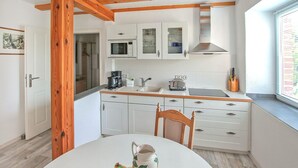 A compact kitchen with white cabinets, a built-in microwave, and a window with blinds.