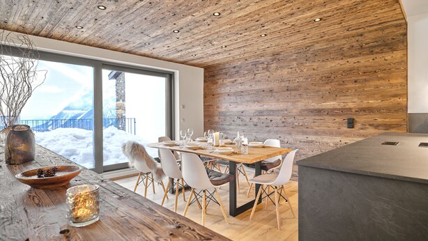 Een moderne eethoek met een houten plafond, grote ramen en uitzicht op een besneeerd landschap.