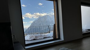 Een kamer met een groot raam met uitzicht op een besneeuwd berglandschap.