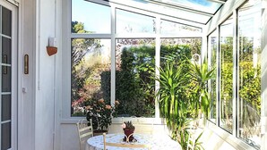 A conservatory with a glass ceiling, a round table with chairs, and potted plants. - Stunning home in Tabre (Tabre)