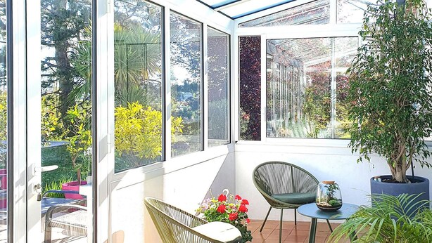 A sunlit room with large windows, a chair, a small table, and a potted plant. - Stunning home in Tabre (Tabre)