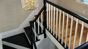 A staircase with black and white railings, a clear glass pendant light, and patterned wallpaper.