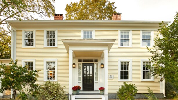 A two-story house with a front porch, steps leading to the door, and a small garden area with shrubs and flowers.