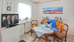 A living room with a television, a sofa, a coffee table, and a painting of Miami Beach. - Ferienhaus Waren (Müritz) (Waren (Müritz) OT Ware)