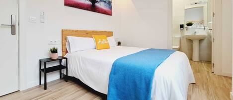 Un dormitorio moderno con cabecera de madera, ropa de cama blanca, un plaid azul y un cuadro colgado en la pared con un árbol.