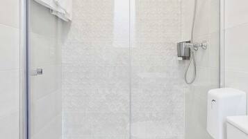 Cabina de ducha con paredes de vidrio, cabezal de ducha de mano y grifo empotrado.