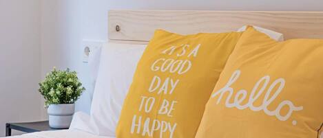A bed with two pillows, one with "It's a good day to be happy" and the other with "hello."