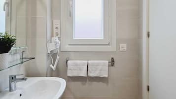 A bathroom with a white sink, a mirror, a window, and a towel rack.