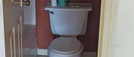 A small bathroom with a toilet, a towel rack with two towels, and a door.