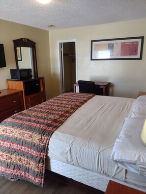 A hotel room with a bed, a desk, a chair, a wardrobe, a mirror, and a framed picture on the wall. - Rolling Fork Motel (Rolling Fork)
