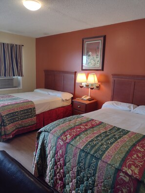 A hotel room with two beds, each with a patterned bedspread, a nightstand with a lamp, and a framed picture on the wall. - Rolling Fork Motel (Rolling Fork)