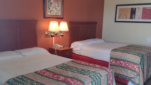 A hotel room with two beds, each with a patterned bedspread, a nightstand with a lamp, and a framed picture on the wall. - Rolling Fork Motel (Rolling Fork)