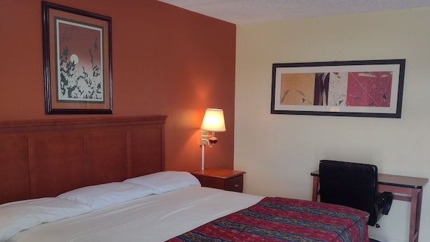 A hotel room with a large bed, a desk, a chair, a nightstand with a lamp, and two framed pictures on the walls. - Rolling Fork Motel (Rolling Fork)