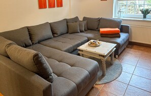 Un canapé modulable avec plusieurs coussins, une petite table agrémentée d’un objet décoratif et une fenêtre donnant sur un paysage verdoyant.
