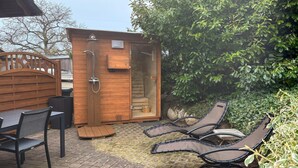 Una sauna de madera con puerta de vidrio, un banco de madera y dos sillones reclinables.