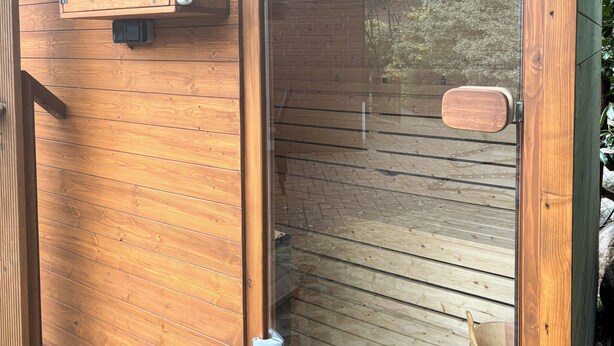 Pared exterior de madera con una puerta metálica y una pequeña ventana.