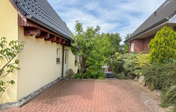 Une cour avec un chemin pavé, un bâtiment jaune doté d’un toit en tuiles et une végétation luxuriante tout autour.