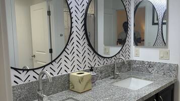 A bathroom with two sinks, a mirror, and a towel dispenser.