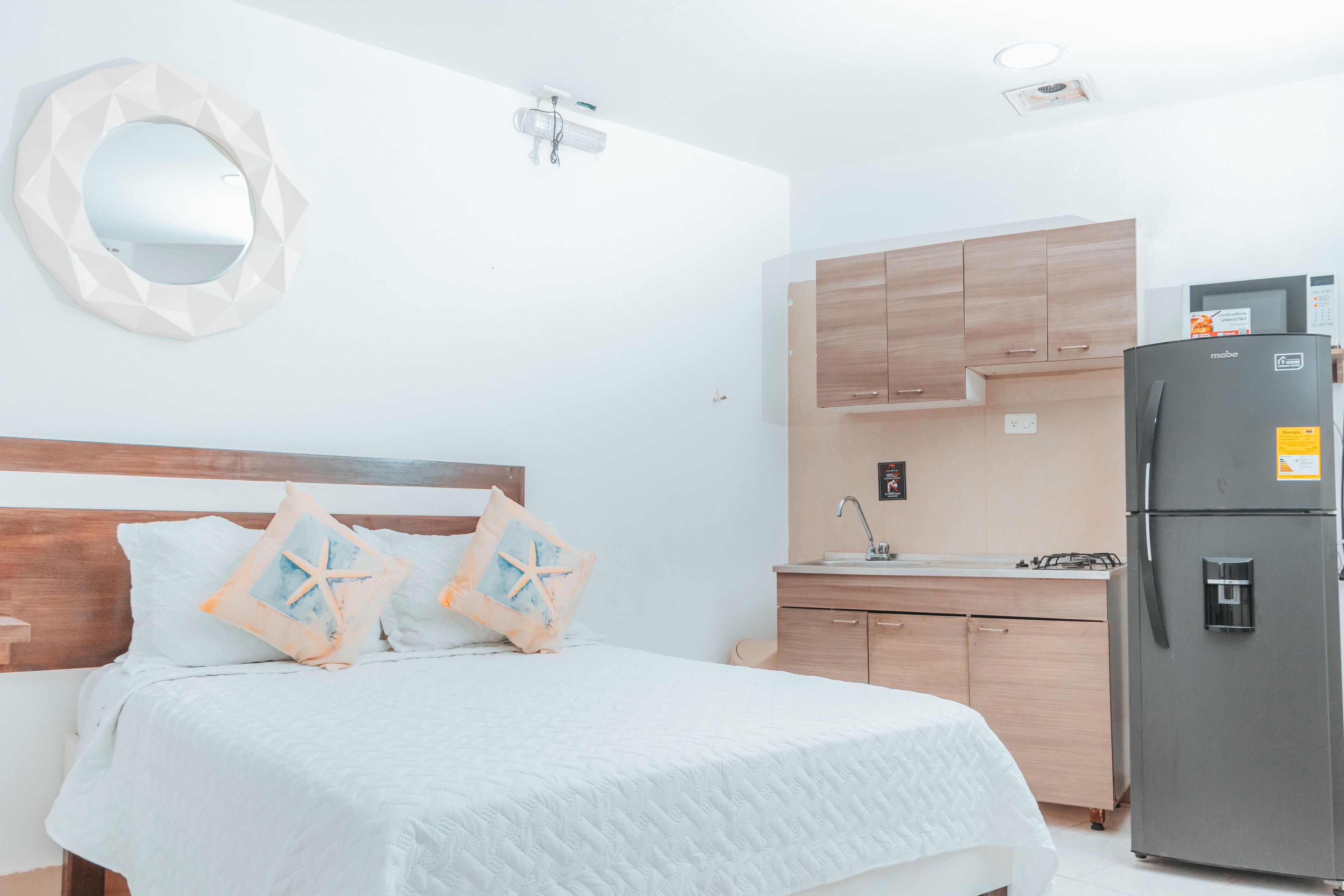 Un dormitorio con cama, mesita de noche, espejo y una kitchenette equipada con refrigerador.