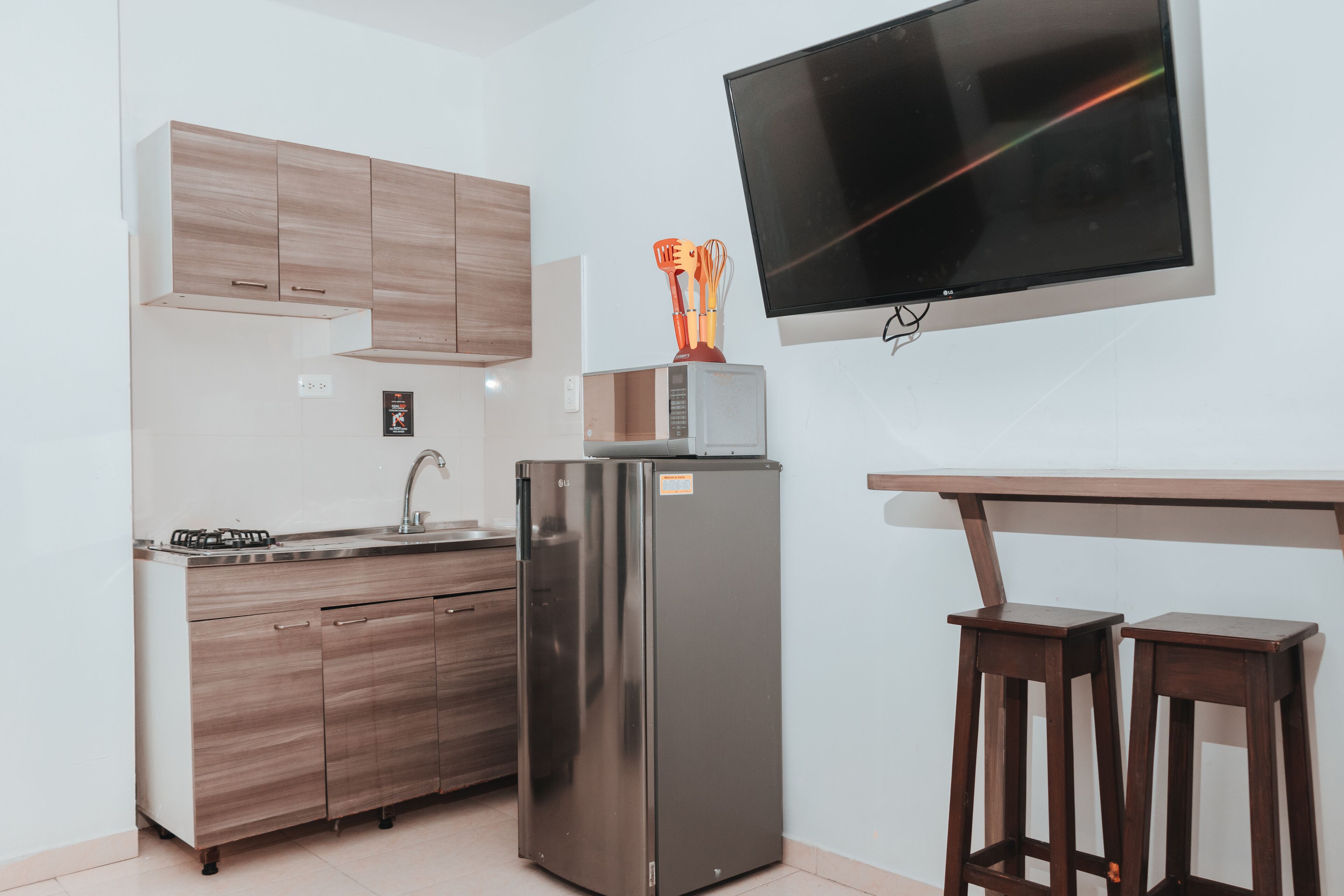 A modern kitchen with a built-in microwave, stainless steel refrigerator, wooden cabinets, a sink, and a bar stool.