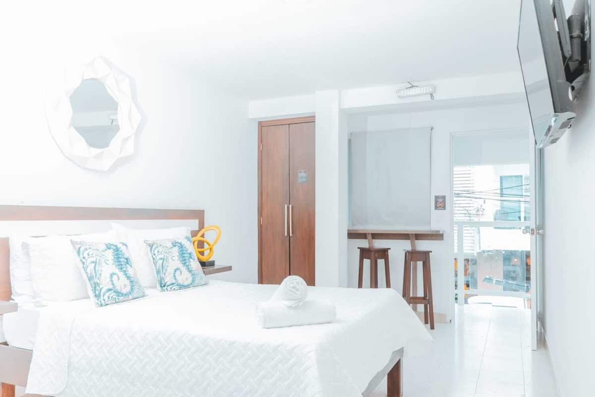 Una habitación de hotel con una cama, un armario de madera, un escritorio y un ventanal grande.