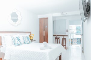 Habitación de hotel con cama, armario de madera, una mesita con silla y balcón con vistas.