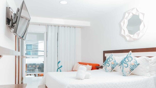 A hotel room with a bed, a TV mounted on the wall, a balcony with a railing, and a view of the outside. - BEIRUT INN (San Andrés)