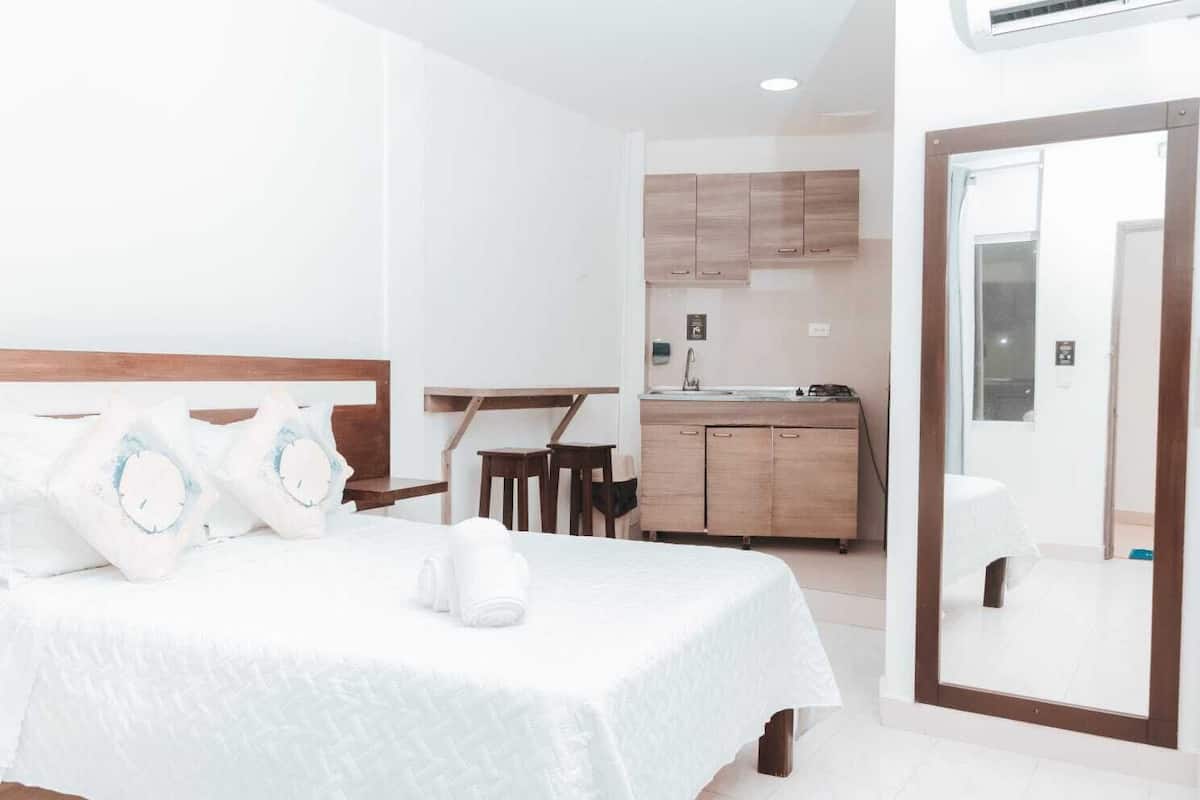 Una habitación de hotel con cama, un escritorio pequeño, una silla, una kitchenette y un baño.