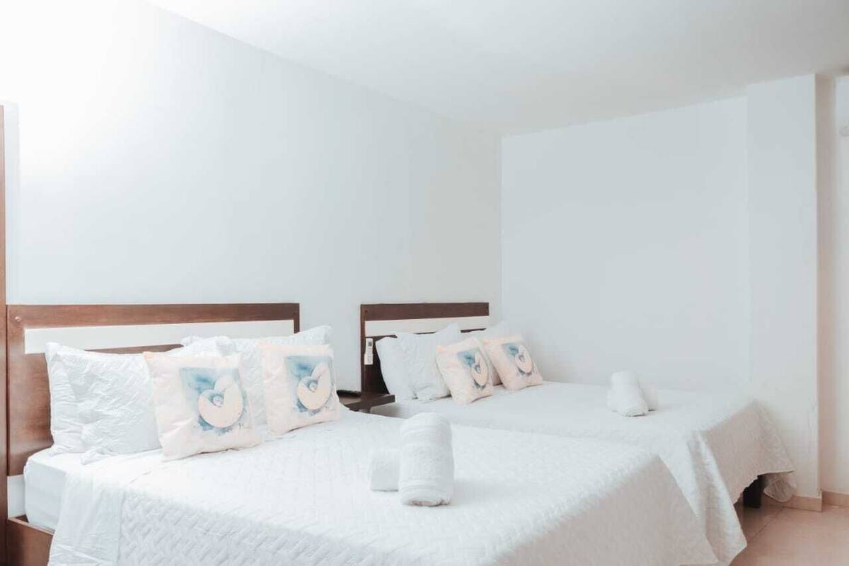 Habitación de hotel con dos camas, cada una con ropa de cama blanca y almohadas a juego.