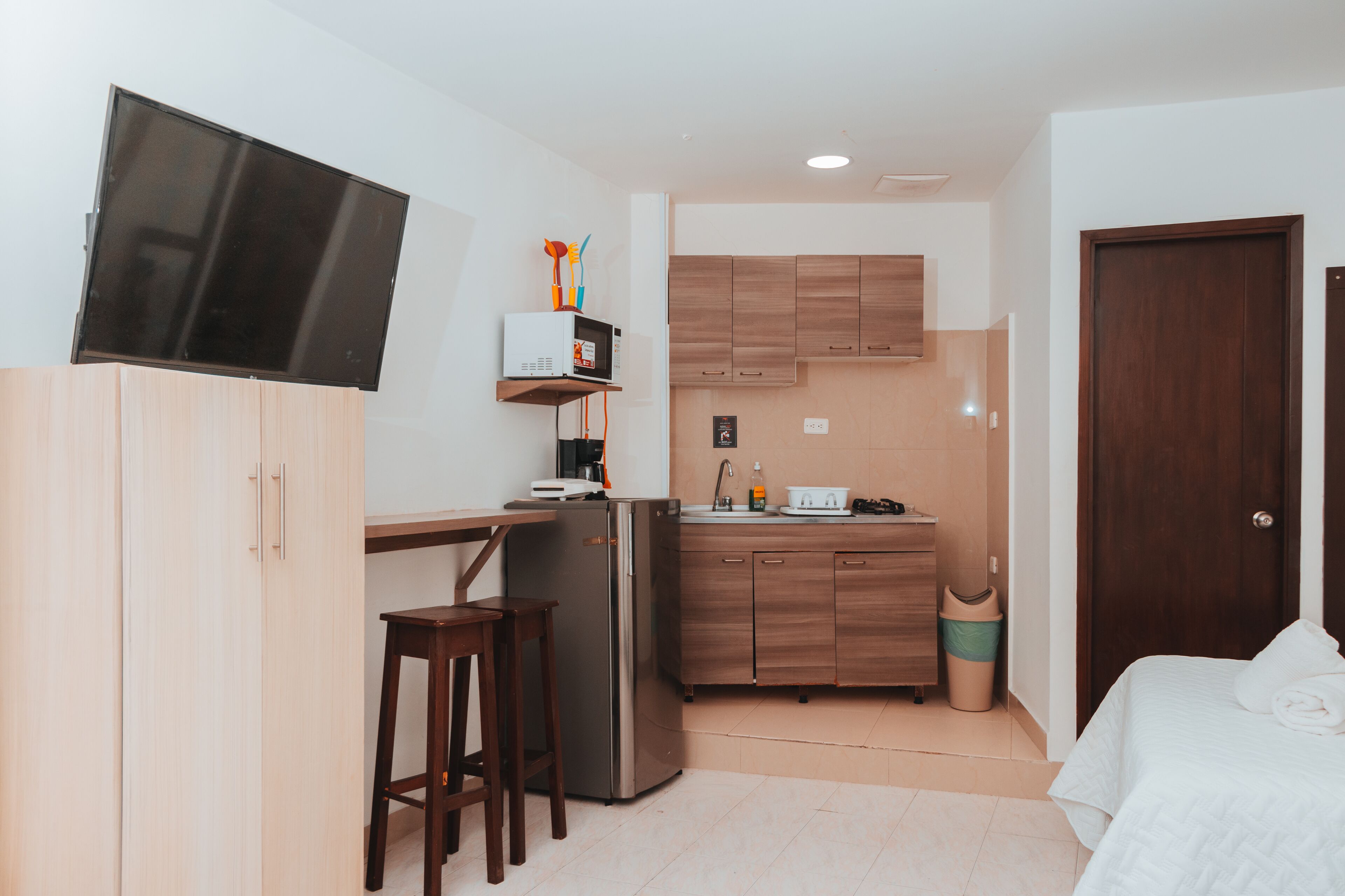 Una habitación compacta con kitchenette, cama, televisor y un pequeño espacio para sentarse.