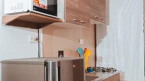 A compact kitchen with a stainless steel refrigerator, a microwave on a wooden shelf, a gas stove, and a trash bin. - BEIRUT INN (San Andrés)