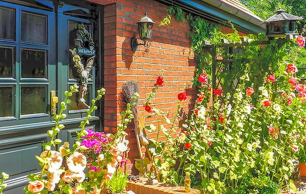 Een bakstenen gebouw met een raam en een deur, een bakstenen muur met een kleine tuin, en een metalen lantaarn.
