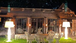 Eine rustikale Holzhütte mit Natursteinfassade, einer Holzdielenveranda und Gartenmöbeln mit Stühlen und Tisch.