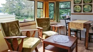 Ein gemütliches Zimmer mit zwei Holzstühlen, einem kleinen Tisch mit Tischdecke und Blick auf Grün hinter großen Fenstern.