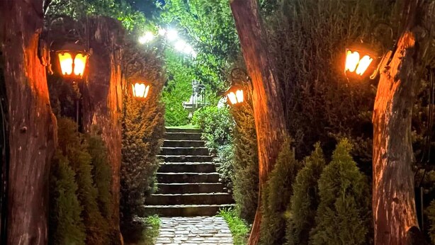 Eine steinerne Treppe, gesäumt von Bäumen und beleuchtet von Laternen, die zu einer höheren Lage führt.