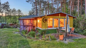 A cozy cabin with a large window, a patio with chairs, and a garden. - Ferienhaus Rheinsberg OT Kagar (Rheinsberg OT Kagar)