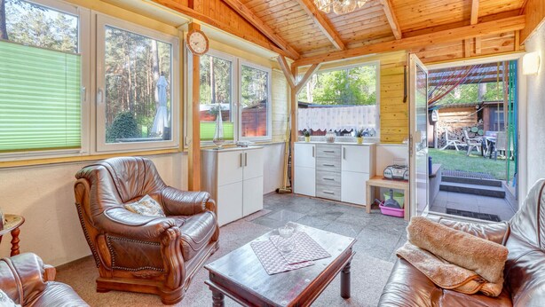 A cozy room with leather sofas, a wooden ceiling, and large windows offering a view of the outdoors. - Ferienhaus Rheinsberg OT Kagar (Rheinsberg OT Kagar)