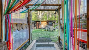A rustic wooden structure with colorful fabric hanging, a small wooden table and chairs, and a metal gate leading to a grassy area. - Ferienhaus Rheinsberg OT Kagar (Rheinsberg OT Kagar)
