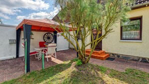 A patio with a table and chairs, a small tree, and a building with a window. - Ferienwohnung Wesenberg (Wesenberg OT Strasen)